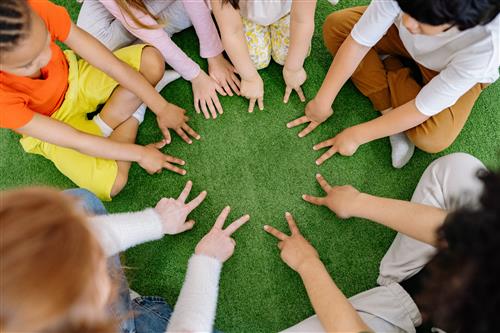 Kids in a circle with arms stretech out forming a circle with their hands and having the "Peace" Sign up.